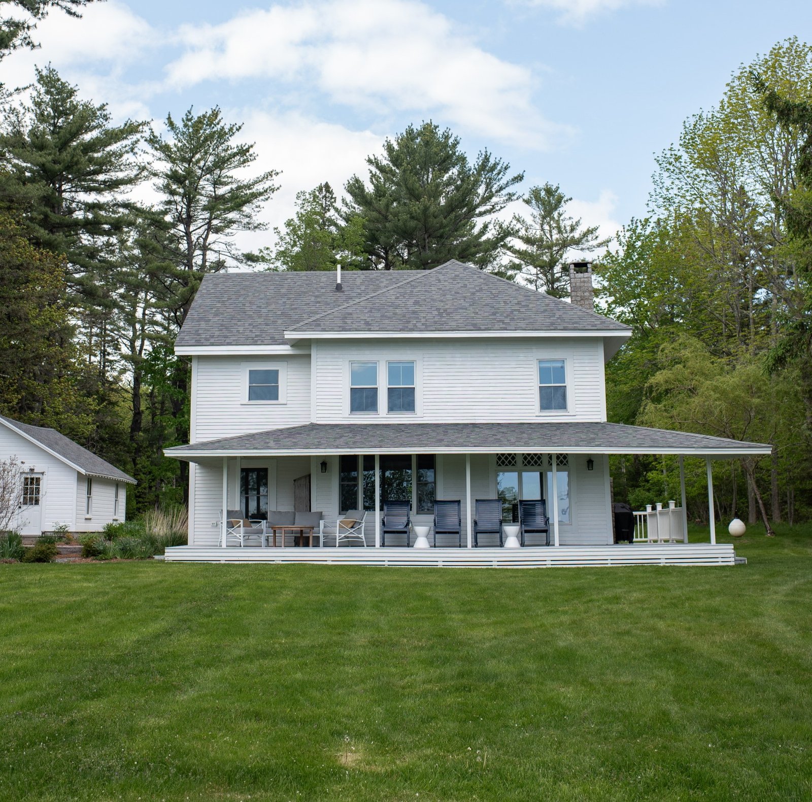 Antique house with overhanging porch and spacious multiple stories painted white surrounded by green grass