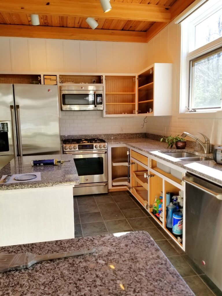 A progress shot of the kitchen with white cabinets and marble tops, as the cabinet doors are missing