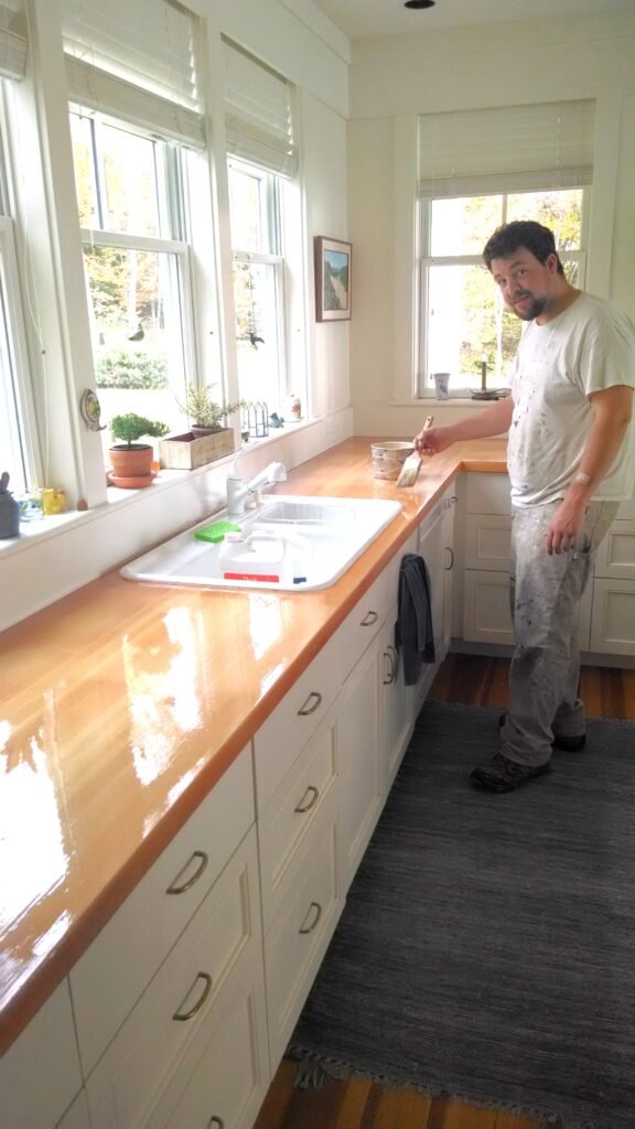 Crew member adding varnish to the top of a counter to go with the newly painted cabinets and walls