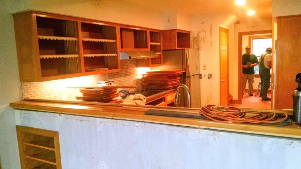 A before shot of a kitchen in progress, with cabinet doors removed and walls peeling.