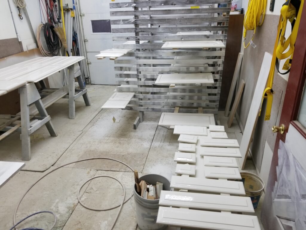Cabinet doors have a fresh coat of white paint and are laying out to dry in a workshop