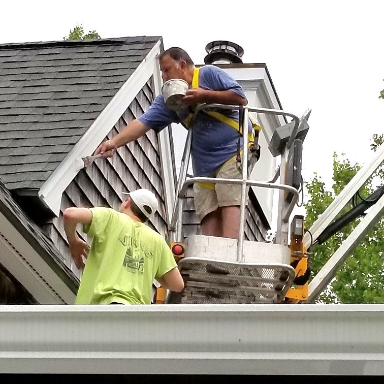 Michael working alongside a crew member painting the trim white on a house