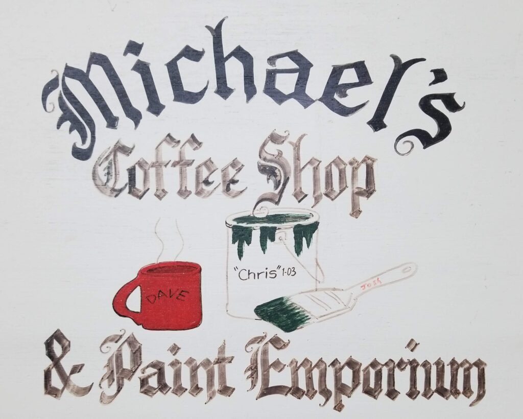 A handpainted sign made by Mike's brother-in-law that hangs in the private workshop of Michael's Painting that says "Michael's Coffee Shop & Paint Emporium"