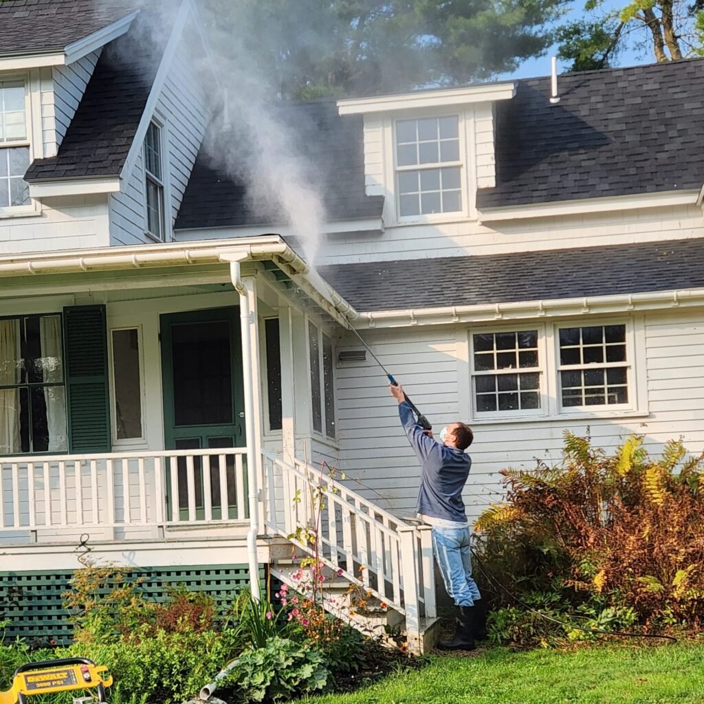 Crew member power washing the exterior of an older white house to remove residue and ensure a clean paint job
