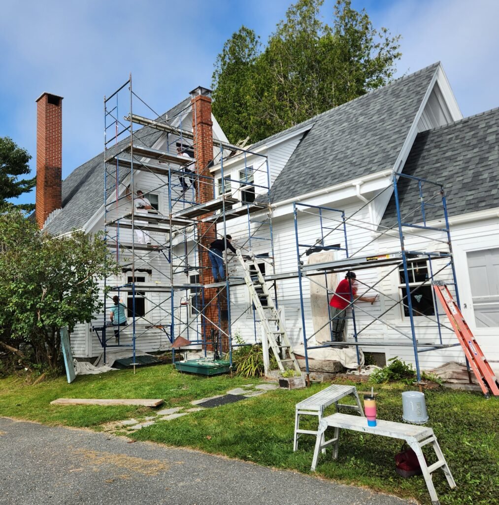 Crew painting on multiple levels of staging on the exterior of a large white house
