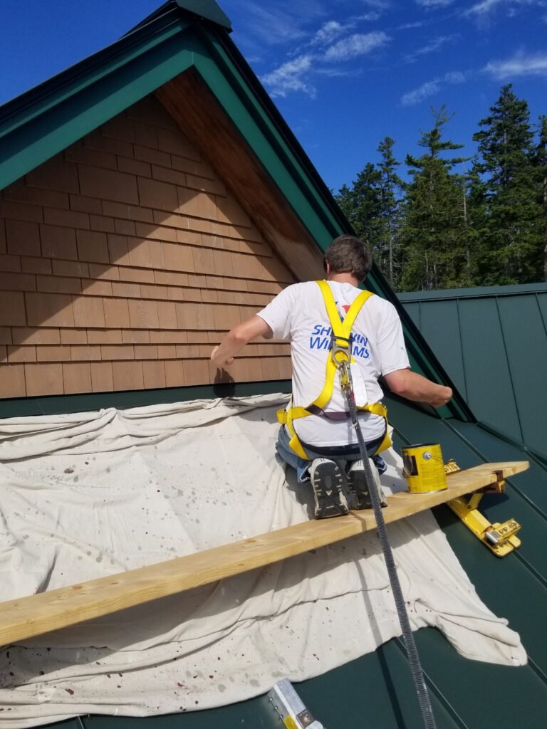 Crew member on roof adding paint details around green trim