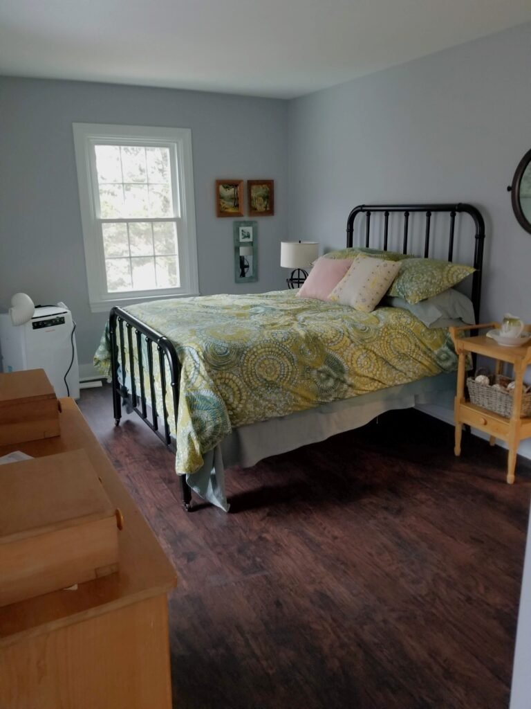 A green antique bed in a freshly painted bedroom with blue hued walls and dark wooden floors