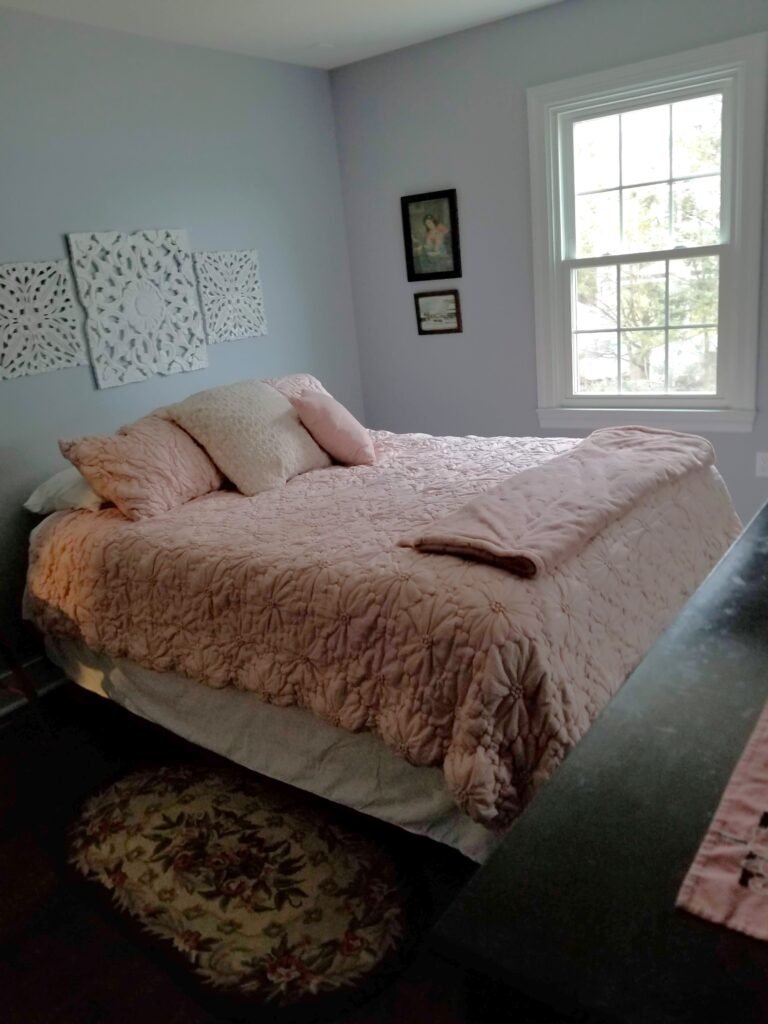 A freshly made pink bed in a bedroom with soft blue walls looks inviting for company.