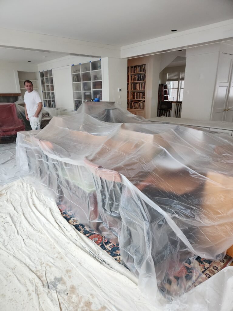 Worker smiles at plastic covering homeowner furniture and tarps on the floor that will protect the home from damage or stains during the painting process