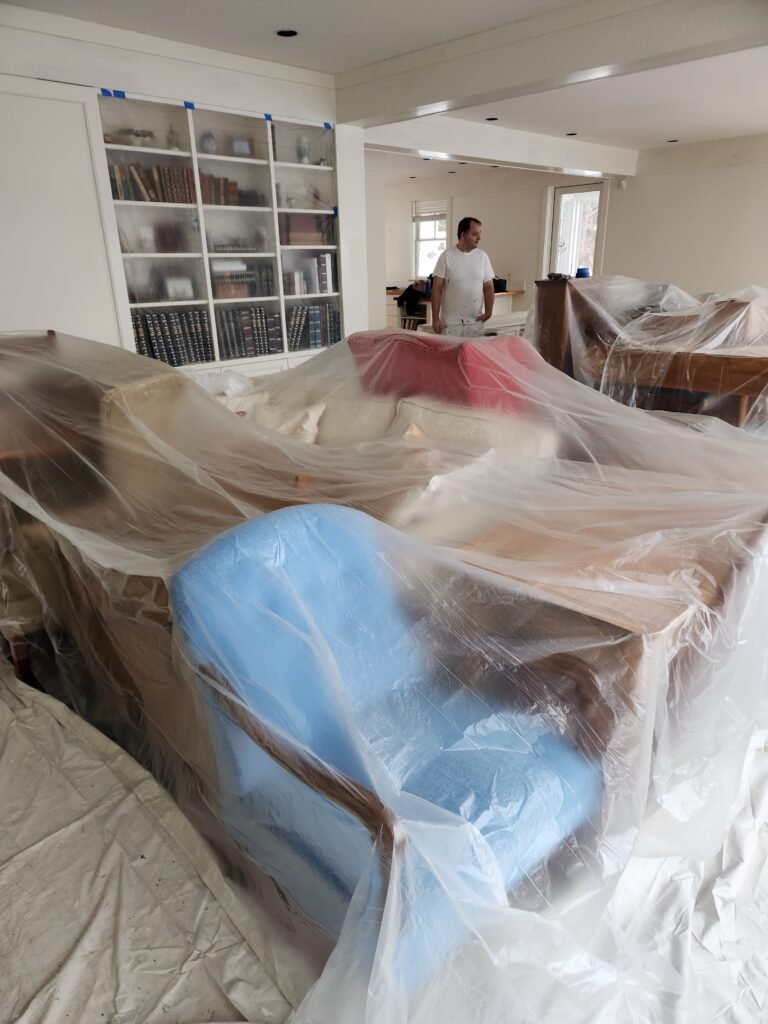 Photo depicts a crew member preparing for work while all homeowner furniture has been covered with plastic film to prevent paint and other residue from causing a mess.