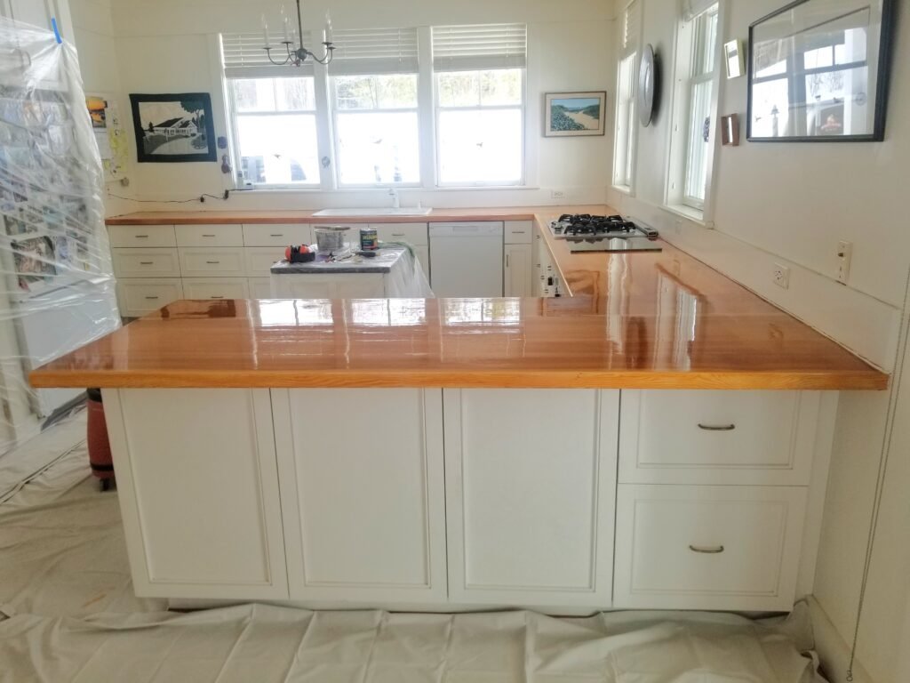A long white island of cabinets in a freshly painted white kitchen with a newly varnished wooden top