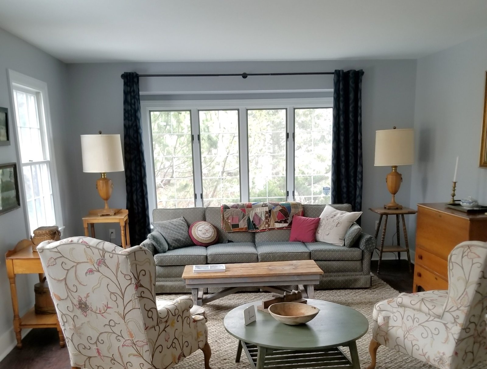 A modern living room with cool grey walls, a long four seat couch with throw pillows, and plenty of windows to view the outside